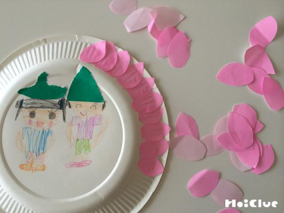 紙皿のふちにピンクの花びらの形に切った折り紙を貼り付けている写真