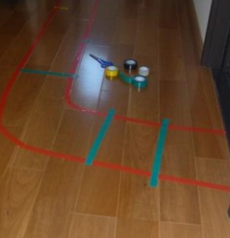 床にビニールテープを貼って線路を作っている写真