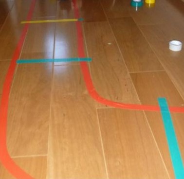 床にビニールテープを貼って線路を作っている写真