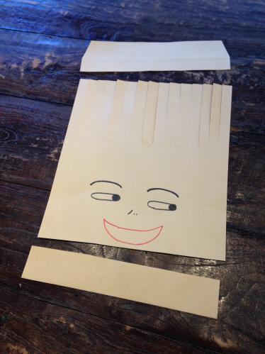 紙袋に顔を描き上下を切り取って前髪の部分に切り込みを入れた写真
