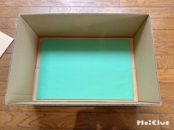 ダンボール箱の底に、芝生に見立てた緑色の画用紙を敷いた写真
