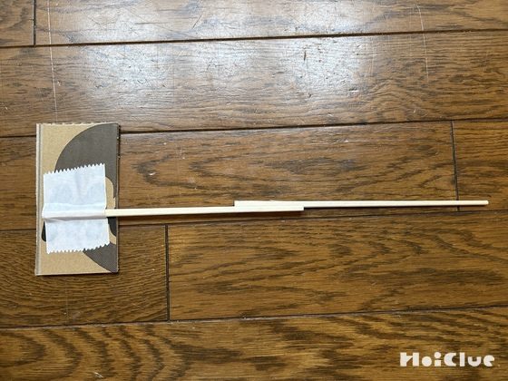 割り箸を2本、重なるようにつなぎあわせ、片方にサッカー選手が描かれたダンボール片板が貼り合わせている写真