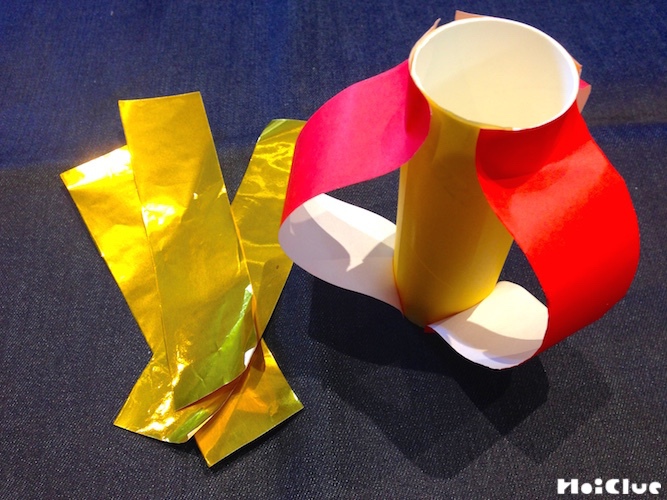 トイレットペーパーの芯の上下部分に折り紙をたわませる様に貼り付ける様子